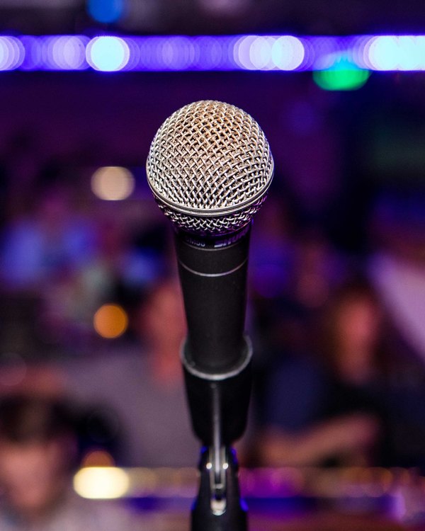 A microphone facing a blurred comedy club crowd.