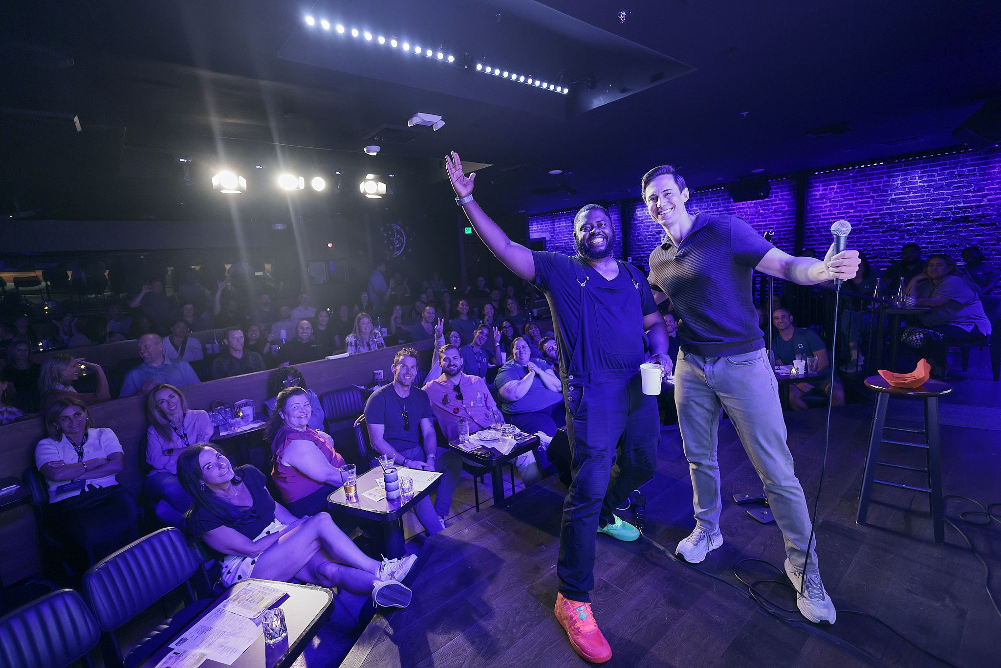 Corey Martin Craig and a comic, arms up, on the Ice House stage in front of a full corporate crowd.