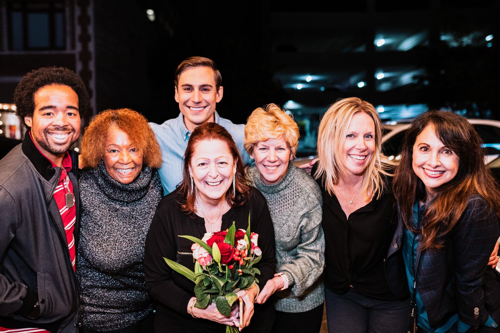 Adult students and Corey smiling together outside the Ice House after a showcase, one holding flowers.